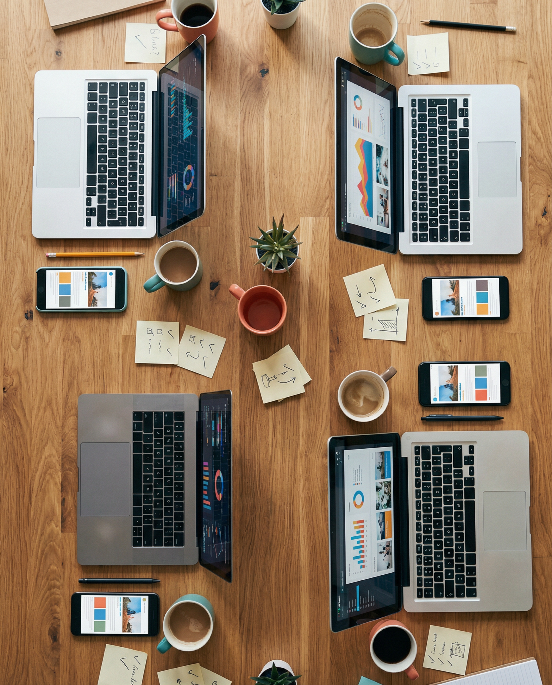 Photorealistic editorial photograph: aerial top-down view of collaborative workspace table showing the aftermath of successful AI implementation, multiple open laptops displaying various content forma