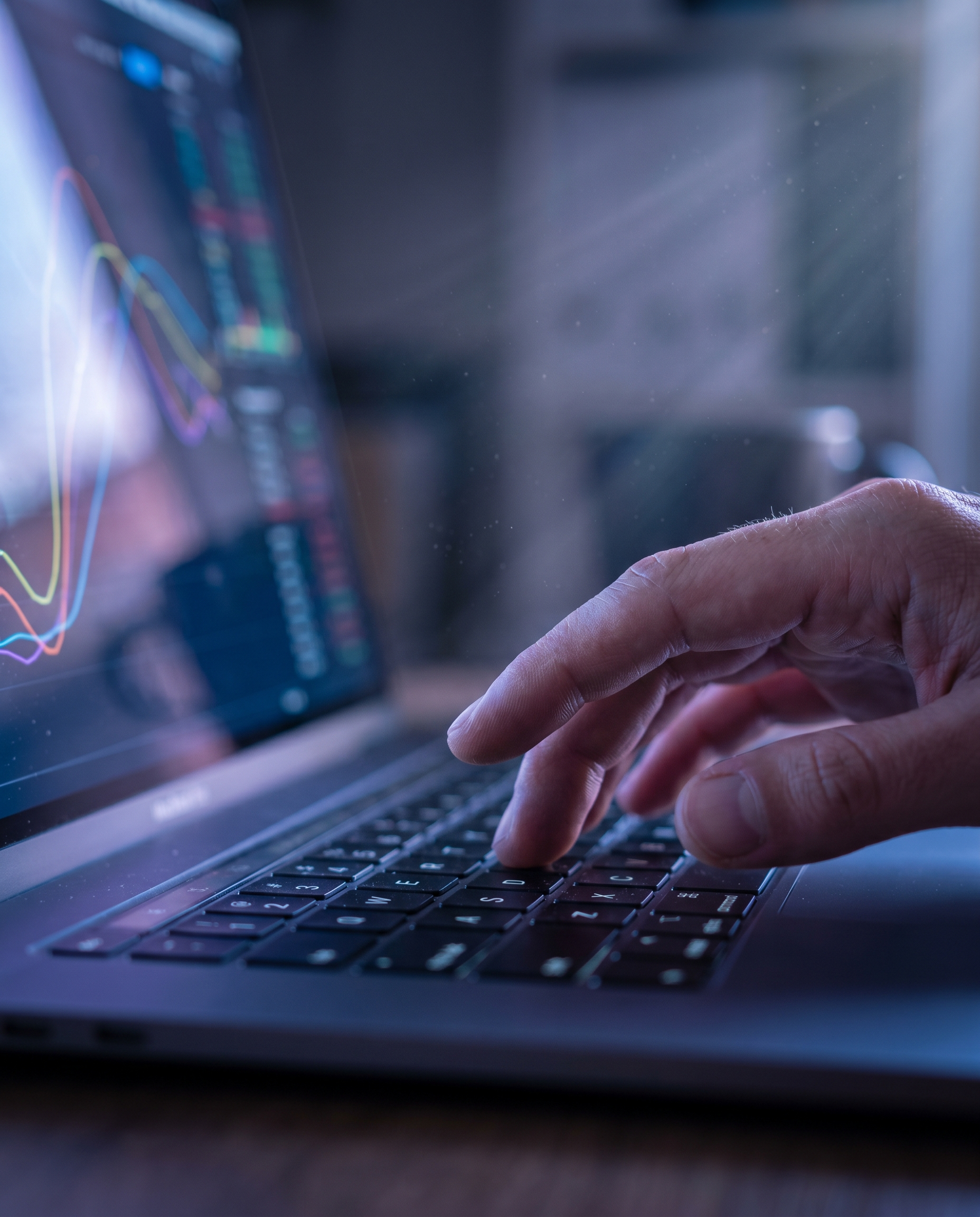 Photorealistic close-up editorial photograph: human hand hovering over laptop keyboard frozen mid-type, screen reflecting colorful analytics dashboard with engagement curves, dramatic rim lighting fro