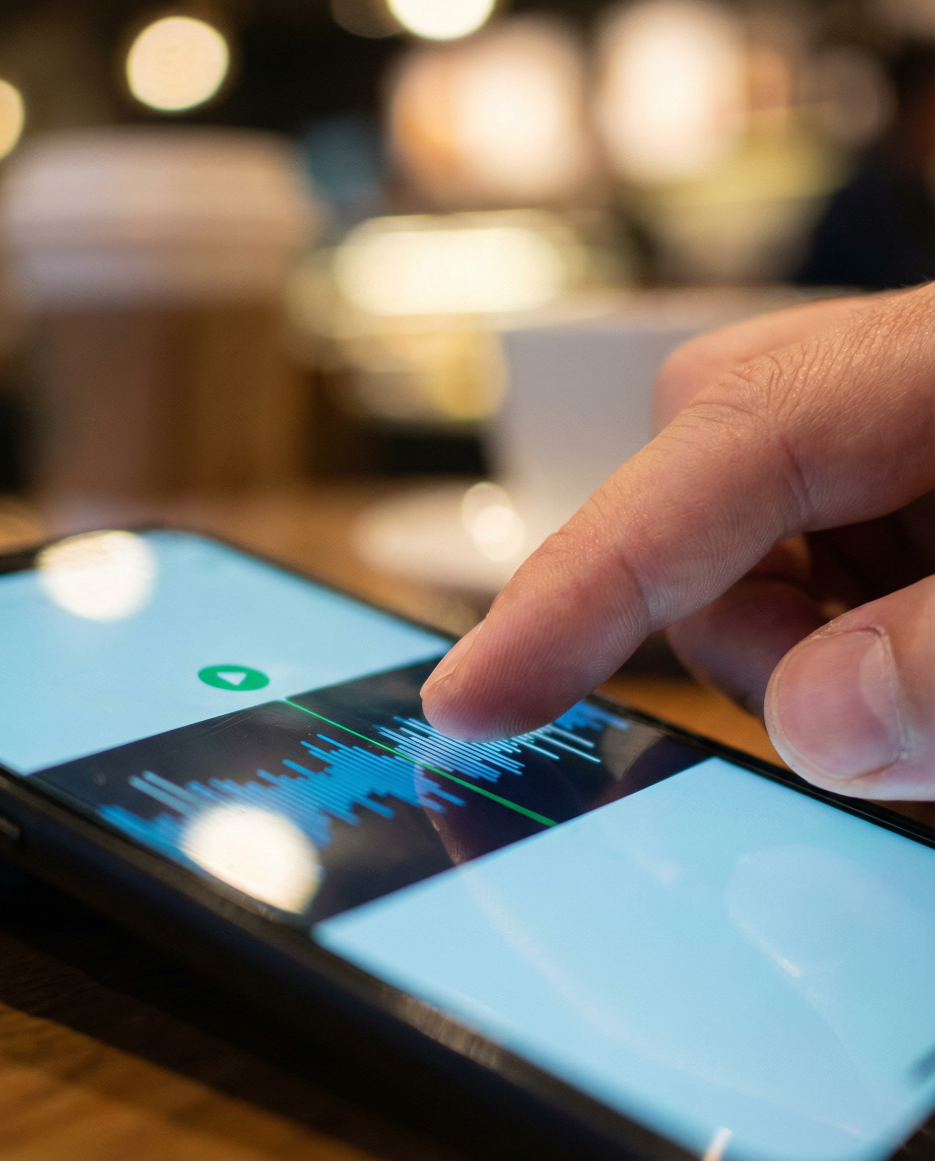 Photorealistic editorial photograph: tight close-up of smartphone screen displaying podcast waveform being edited in real-time, finger swiping across interface, coffee shop environment blurred in back